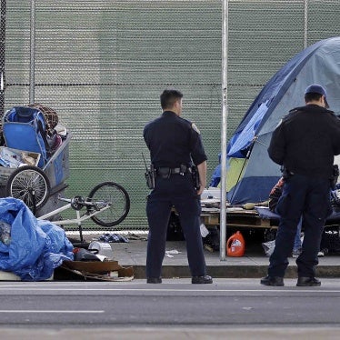 Police officers wait while people experiencing homelessness collect their belongings during a sweep of their encampment under a San Francisco, California freeway, March 1, 2016. 