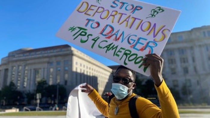 A person holding a protest sign that reads "Stop Deportations to Danger"