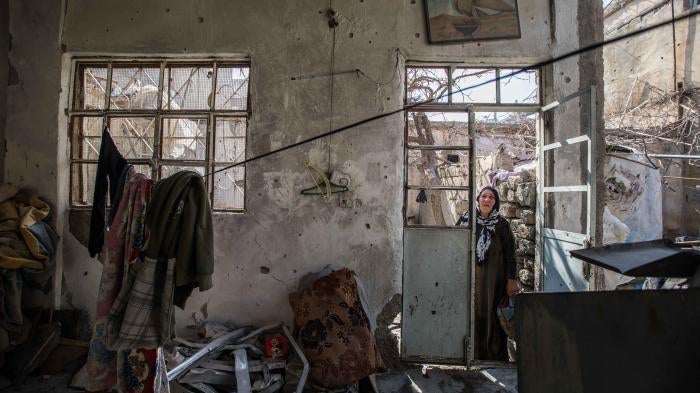 An older woman stands in the doorway of a destroyed home