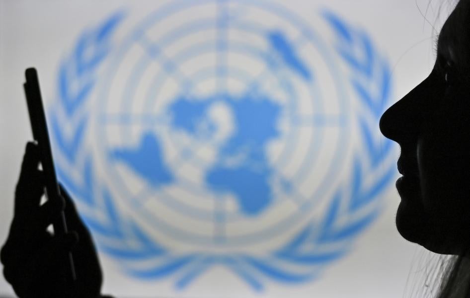 A woman looks at her cell phone in front of the United Nations logo displayed on a computer screen.