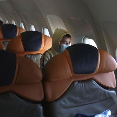 A boy in a face mask sits alone on an airplane