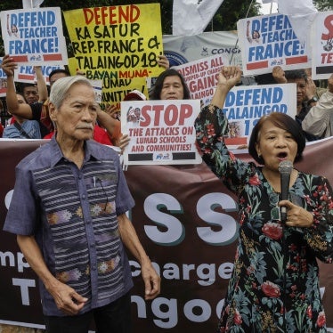 A man and a woman hold microphones in front of a crowd holding protest banners