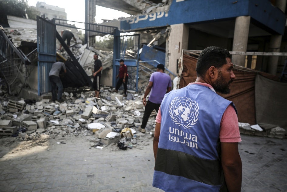 Workers stand in front of the ruins of a school building