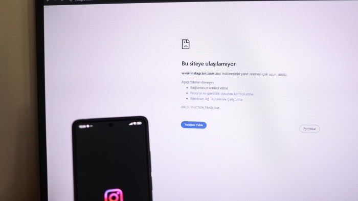 A person holds a phone showing the Instagram logo while a computer screen displays the message “This site can not be reached'”