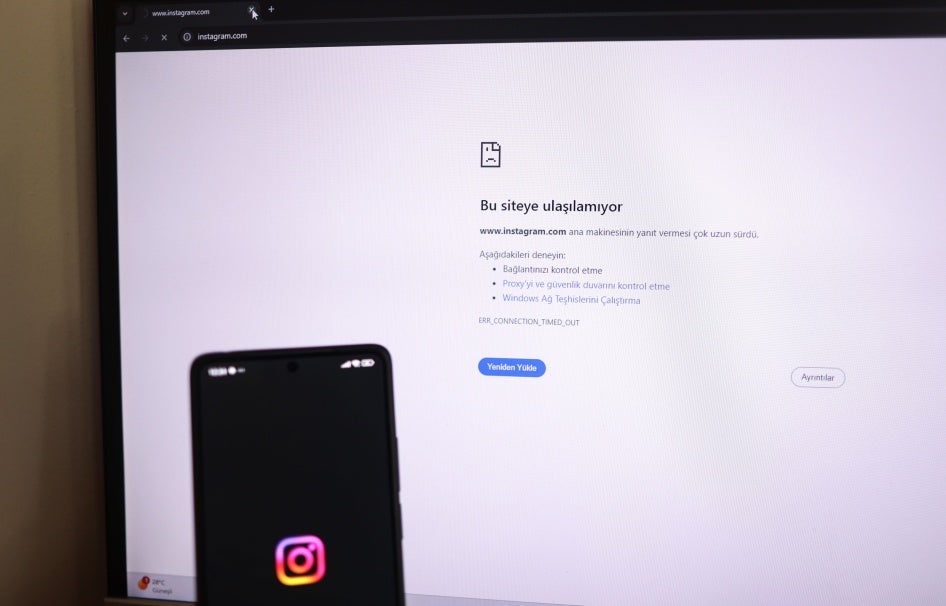 A person holds a phone showing the Instagram logo while a computer screen displays the message “This site can not be reached'”