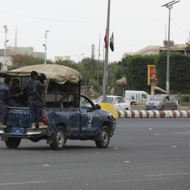 Soldiers in uniform ride in a military vehicle down a city street