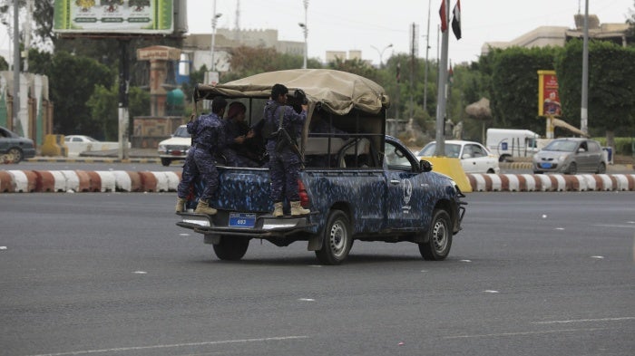 Soldiers in uniform ride in a military vehicle down a city street