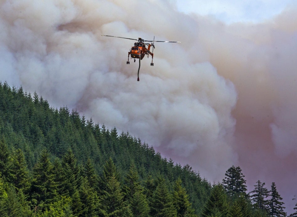 A helicopter flies over a wildfire in a forest